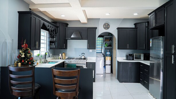 A modern kitchen with dark cabinetry, a central island with two wooden chairs, stainless steel appliances, and a decorative Christmas tree. - Chenko Villas & Cars (Jennings)