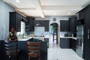A modern kitchen with dark cabinetry, a central island with two wooden chairs, stainless steel appliances, and a decorative Christmas tree.