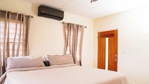 A bedroom with a bed, curtains, a door, and an air conditioning unit. - Chenko Villas & Cars (Jennings)