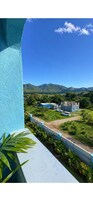 Vista desde un balcón con cielo despejado, un edificio distante que parece un castillo y un paisaje verde.