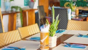 Un comedor con una mesa de madera dispuesta para dos personas, con individuales tejidos y una jarrón de vidrio transparente con una planta.