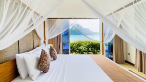 Un dormitorio con una cama grande, cortinas blancas y vistas a una playa y montañas.