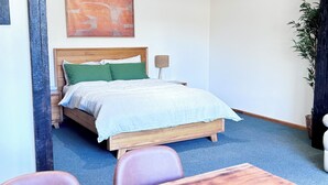 Una cama individual con estructura de madera, almohadas verdes y edredón blanco en una habitación con alfombra azul.