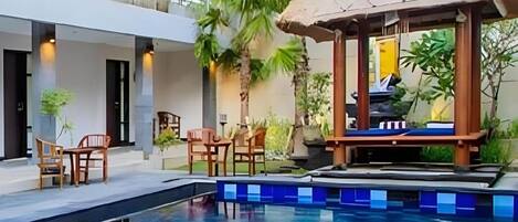 A pool area with a thatched gazebo, lounge chairs, and a small table.