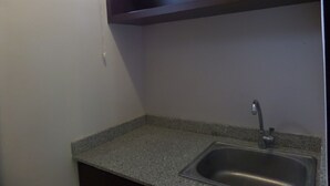 A small kitchen with a granite countertop, a stainless steel sink, and a dark wooden shelf above the sink. - Mansu Hotel & Spa (Denpasar)
