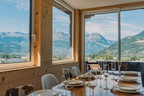 A dining table set for six with a mountain view through large windows. - St Gervais Les Bains - 3 Bed-3 Bath at the Foot of Cable Car (Saint-Gervais-les-Bains)