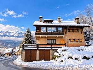 A two-story chalet with a snow-covered roof, a stone chimney, and a wooden fence. - St Gervais Les Bains - 3 Bed-3 Bath at the Foot of Cable Car (Saint-Gervais-les-Bains)