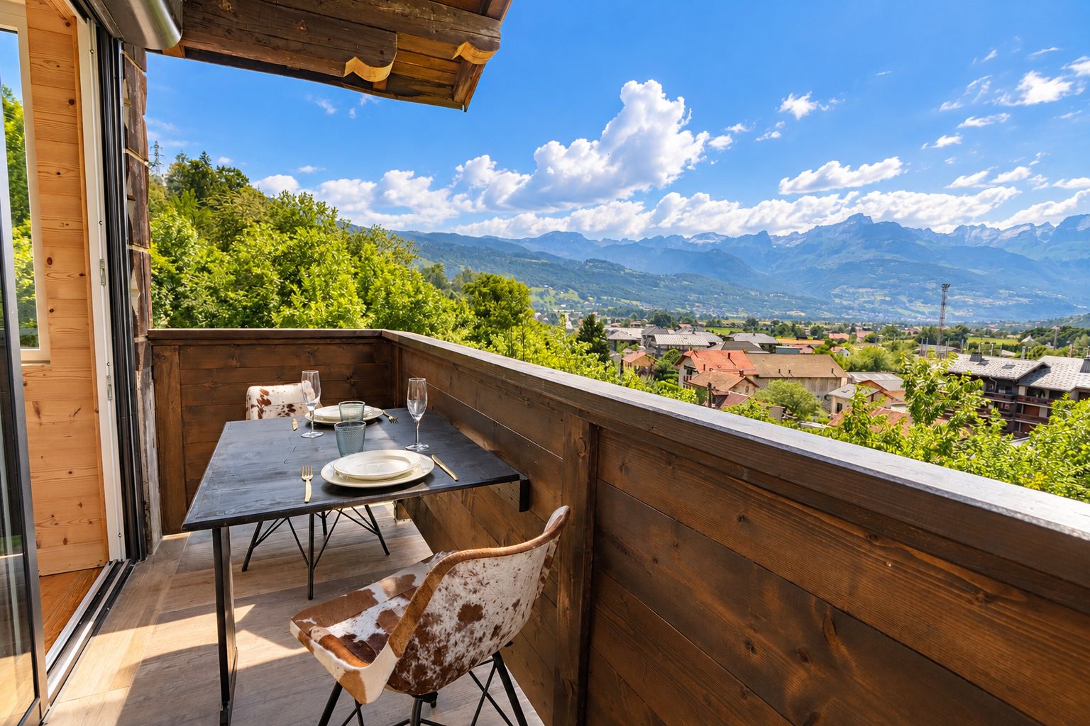 Un balcone in legno con tavolo e sedie, affacciato su un paesaggio montuoso.