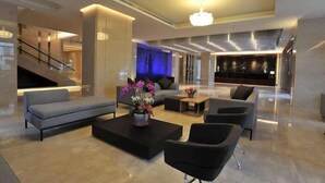 A modern lobby with a sofa, coffee table, and chairs, a staircase, and a reception area with a counter and decorative elements. - Best Hotel (Hualien City)