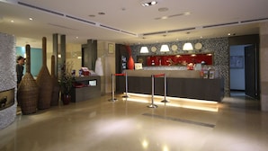 A hotel reception area with a modern design, featuring a reception desk, a clock, and a decorative vase. - Mola Mola Four Seasons Hotel (Hualien City)