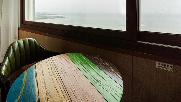 A room with a large window, a round table, and a green chair. - Huesik Hotel Sydney (Jeju City)