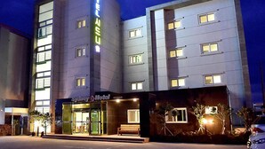 A multi-story hotel with a modern facade, illuminated windows, and a visible entrance with a bench outside. - Huesik Hotel Sydney (Jeju City)