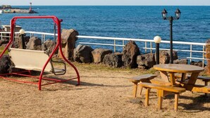 A coastal park with a swing set, picnic tables, and a lamp post. - Huesik Hotel Sydney (Jeju City)