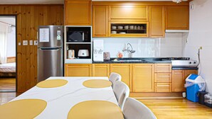 A compact kitchen with wooden cabinets, a built-in microwave, a refrigerator, and a dining table with yellow placemats. - Huesik Hotel Sydney (Jeju City)