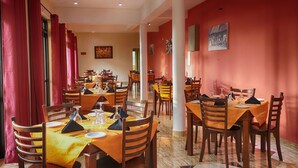 Un comedor con varias mesas y sillas, cortinas rojas y obras de arte en las paredes.