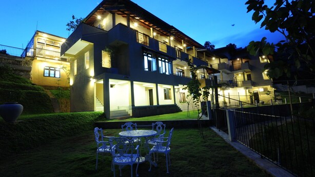 Un edificio de varios pisos con una entrada bien iluminada y una pequeña zona exterior con sillas y una mesa.