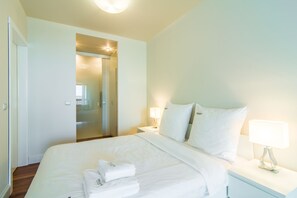 Ein Hotelzimmer mit einem ordentlich bezogenen Bett, einem Nachttisch mit Lampe und einer Tür zu einem weiteren Raum.