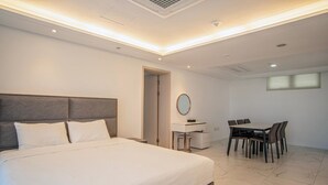 A modern hotel room with a large bed, a desk, and a dining area.