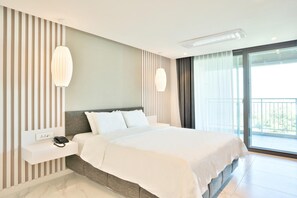 Una habitación de hotel moderna con una cama grande, un teléfono en la mesita de noche, una lámpara de pared y un balcón con vistas.