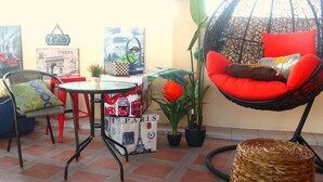 Un espacio al aire libre acogedor con sillas de mimbre, una silla colgante y una mesa con una maleta roja y una caja con motivos de París.