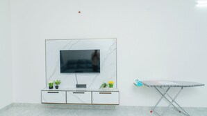 Ett rum med ett TV-bord i marmorimitation, en platt-TV, ett litet bord med ett mönstrat bordsduk och krukväxter.