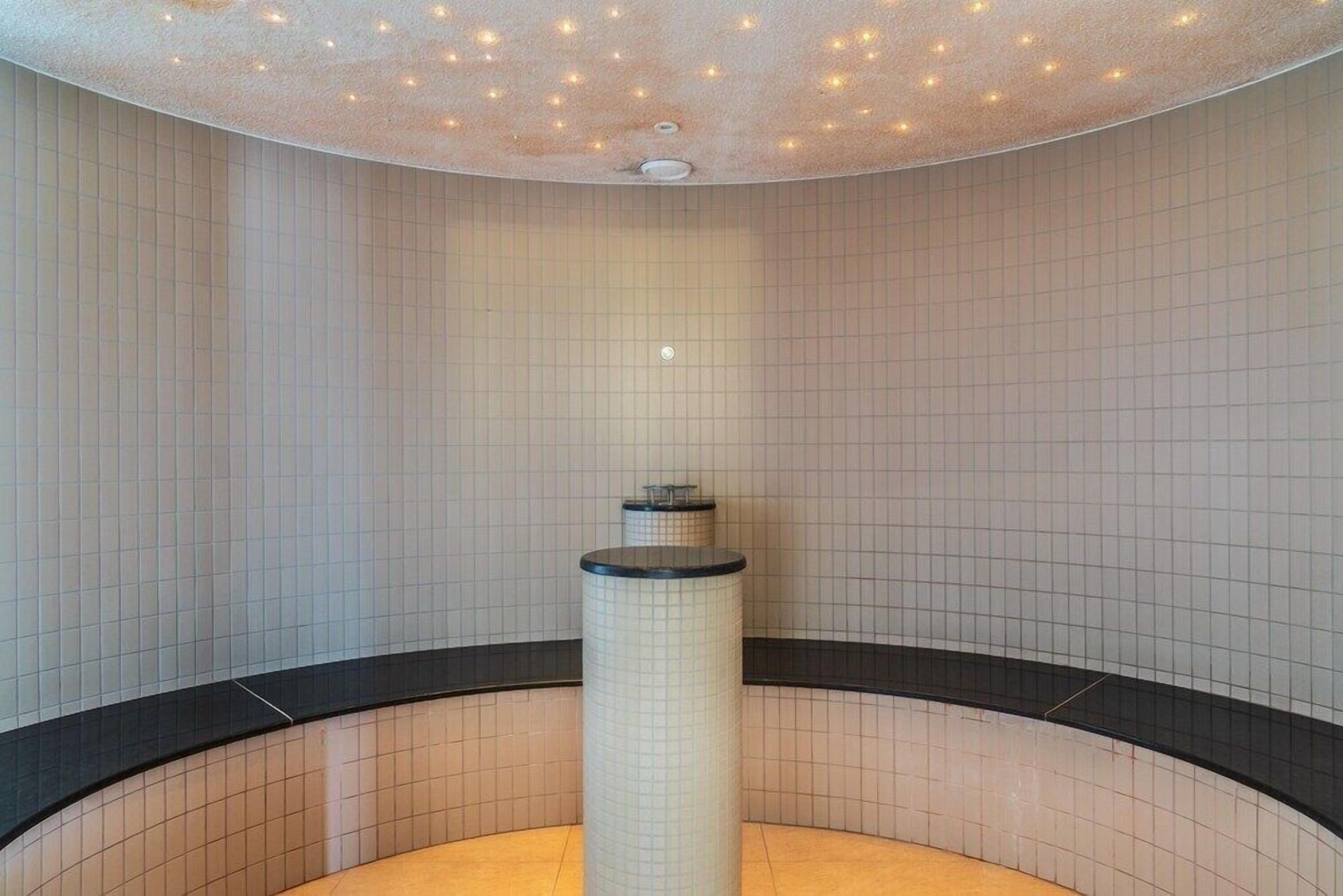 Una habitación circular con suelo y paredes de azulejos, un pilar central y un techo con pequeñas luces.