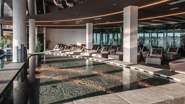 Un espace piscine intérieur moderne, doté de sièges et offrant une vue sur l’extérieur.