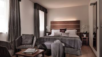 Une chambre d’hôtel avec un grand lit, une chaise, une petite table et une table de chevet avec une lampe.