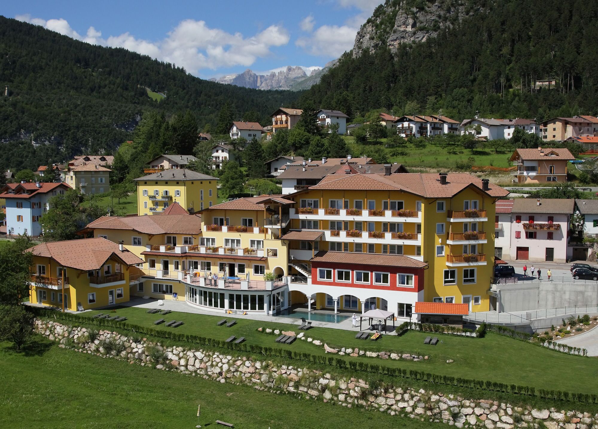 A multi-story hotel with balconies, a swimming pool, and a mountainous backdrop.