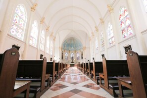 Interior de una iglesia con bancales, vidrieras de colores y suelo a cuadros.