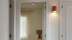 Ein schmaler Flur führt zu einem Schlafzimmer mit einem Bett, einem Nachttisch und einer Lampe.