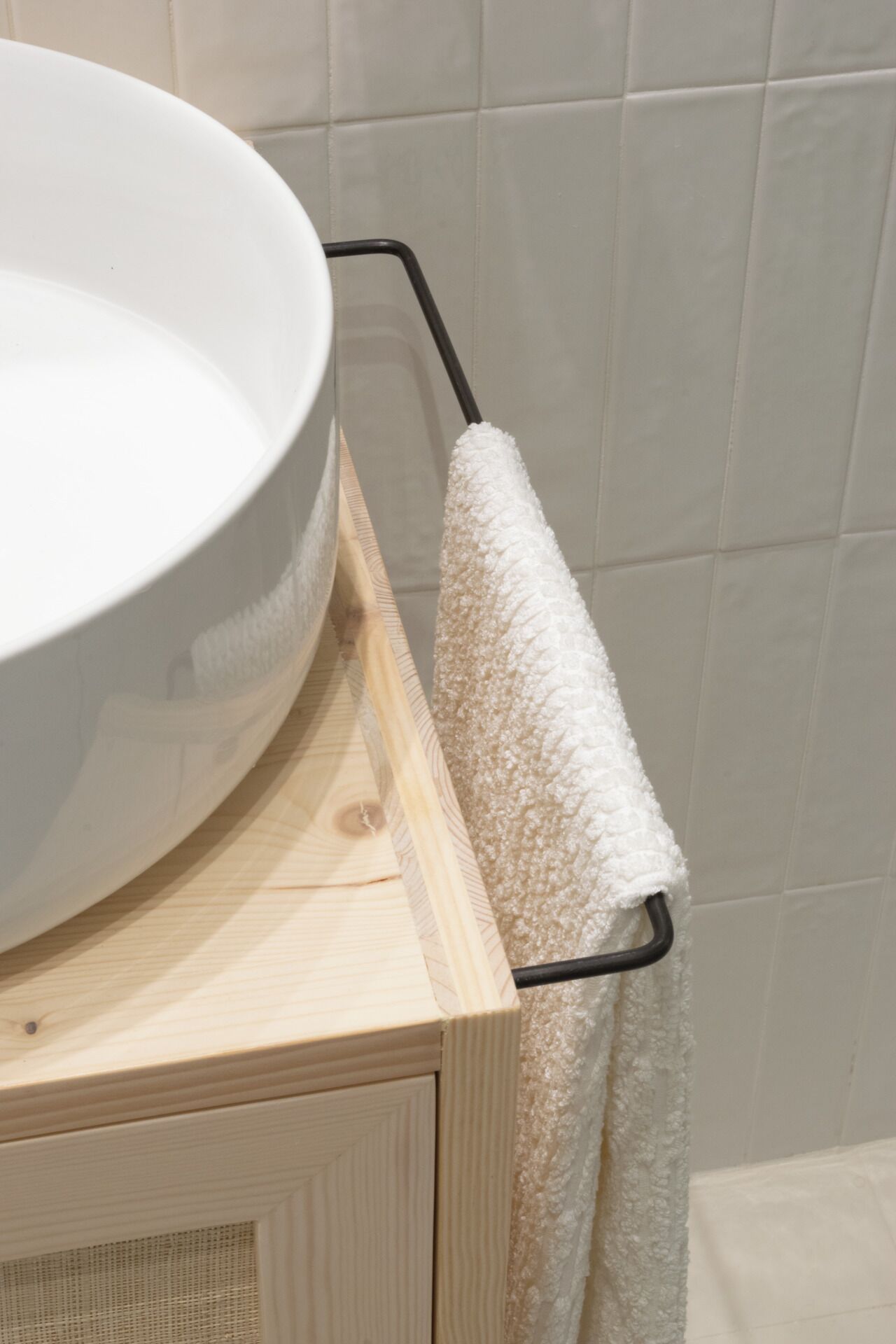Une salle de bain avec un meuble-lavabo en bois, un lavabo blanc et une serviette suspendue à un porte-serviettes en métal.