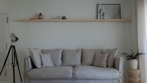 Ein stilvolles Wohnzimmer in neutralen Farben mit einer Couch, einer Stehlampe, einem Spiegel und einem Regal mit Dekoration.