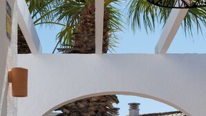 Eine Terrasse mit weißer Wand, einem Reetdach, einem Grill und einem Tisch mit Zitronen.