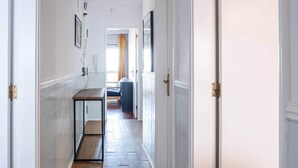 A narrow hallway with a wooden floor, white walls, and a glass partition on one side. - Mivô | Tejo Colours (Almada)