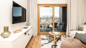 Moderni olohuone, jossa on taulutelevisio, ruokailutila pöytineen ja tuoleineen sekä parveke, jolta on näkymä.