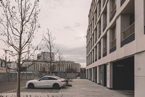 Een modern gebouw met een parkeerplaats, een witte auto ervoor en een boom zonder bladeren.