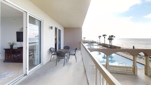En balkong med en pool, en matplats med stolar och utsikt över stranden och havet.