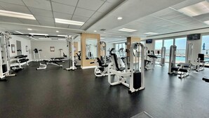 Ett gym med olika träningsmaskiner, stora fönster och utsikt över havet.