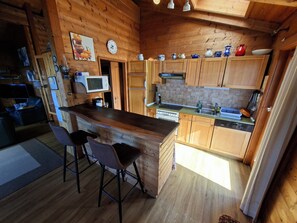 Ett mysigt kök med träskåp, en köksö med barstolar, en mikrovågsugn, en spis och diverse köksredskap.