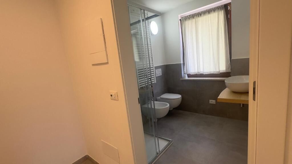 A bathroom with a glass shower enclosure, a toilet, and a sink with a mirror above it.
