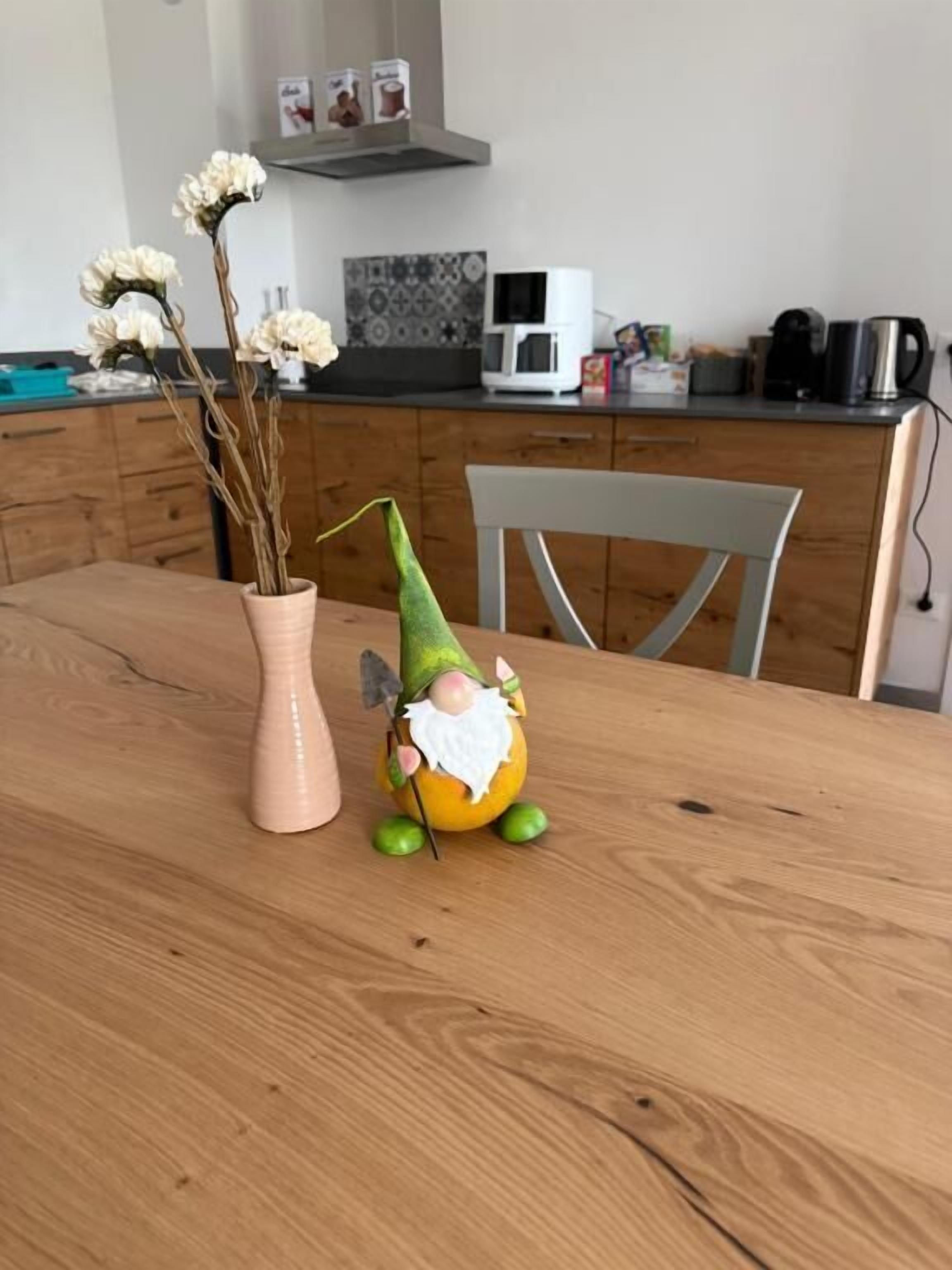 A wooden dining table with a vase of dried flowers and a gnome figurine.