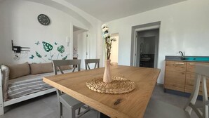 A dining area with a wooden table, chairs, a vase with flowers, and a clock on the wall. - AI 7 NANI (Sedico)