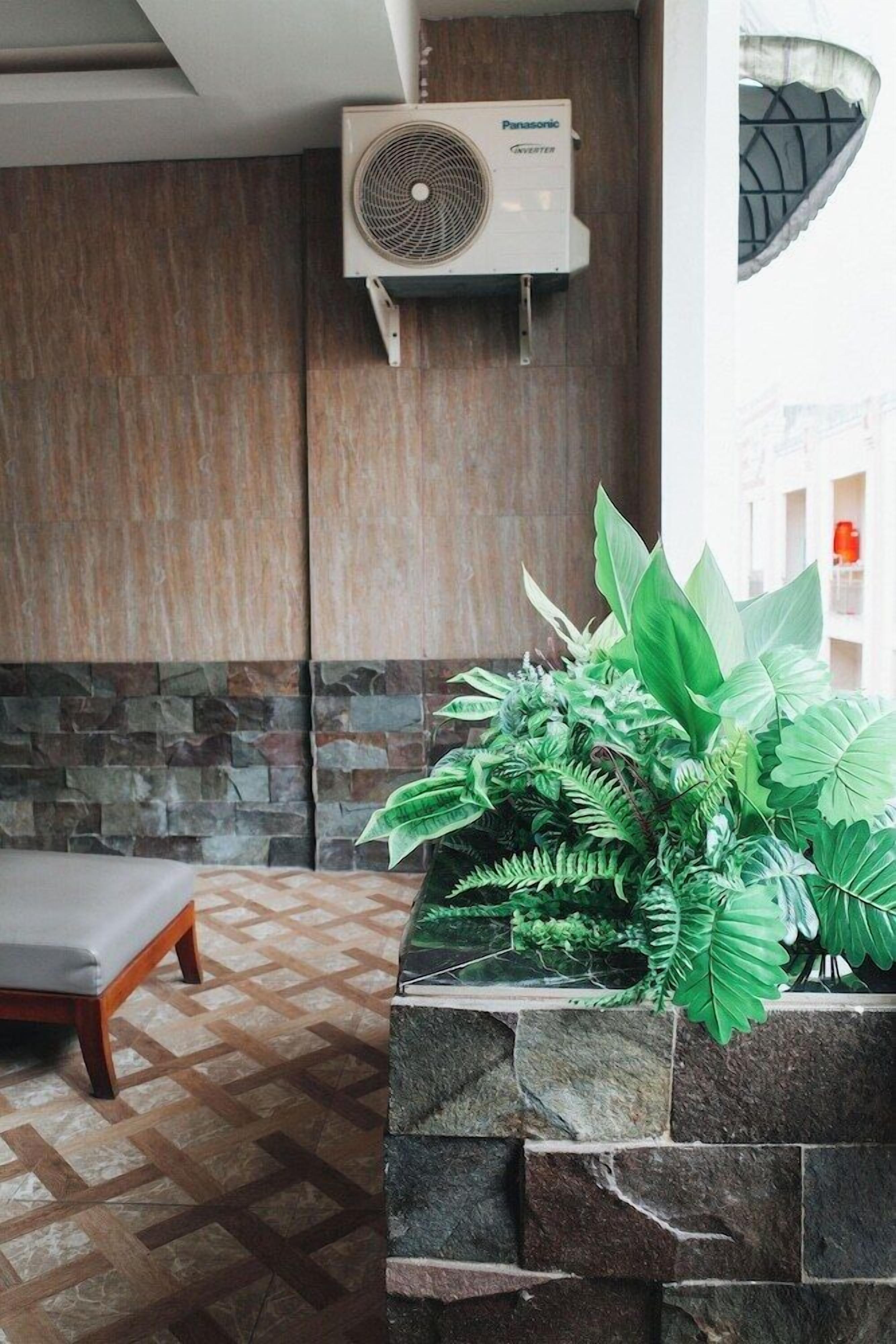 A room with a stone wall, a bed, a large air conditioning unit, and a planter with green plants.