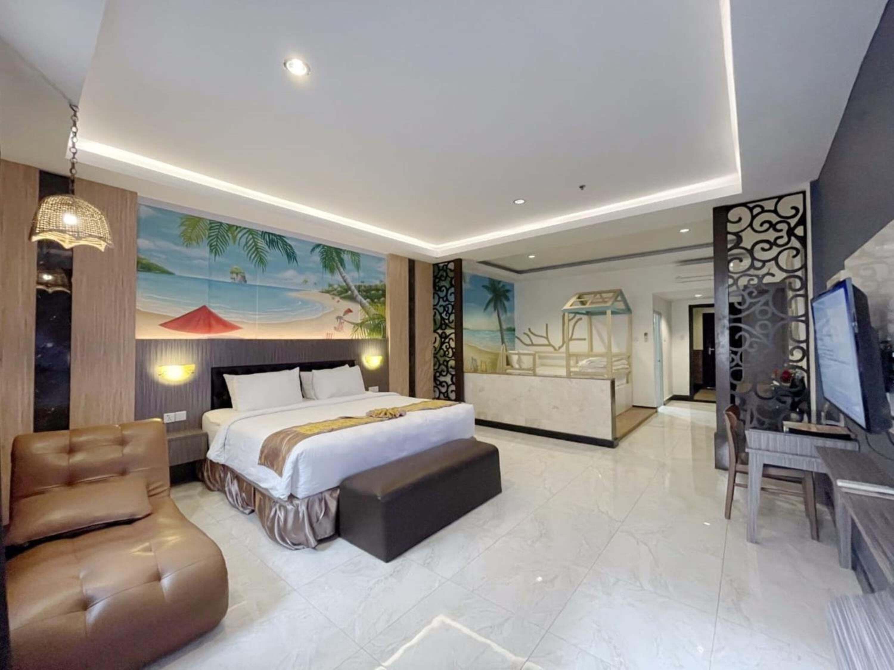 A modern hotel room with a large bed, a seating area, a desk with a computer, and a mural of a beach scene.