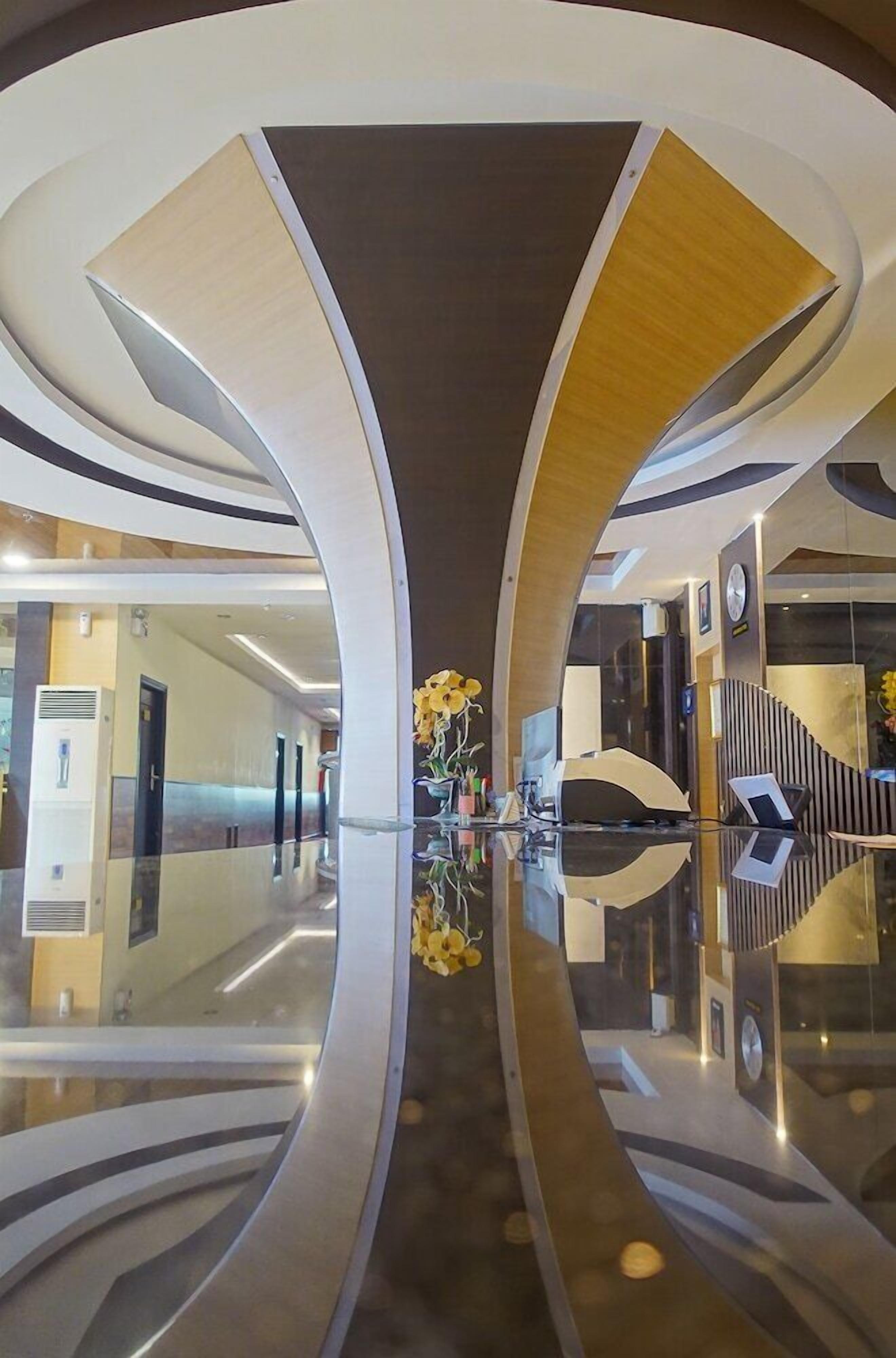 A modern hotel lobby with a reflective floor, curved architectural design, and a central floral arrangement.