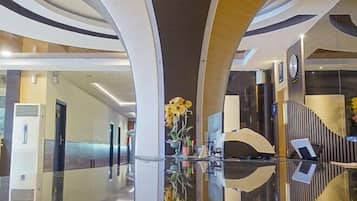 A modern hotel lobby with a reflective floor, curved architectural design, and a central floral arrangement.