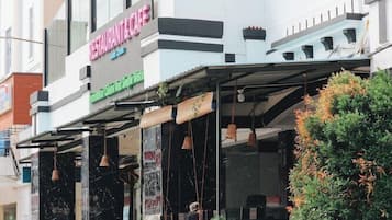A restaurant with a covered outdoor seating area, a signboard, and a small garden with plants.