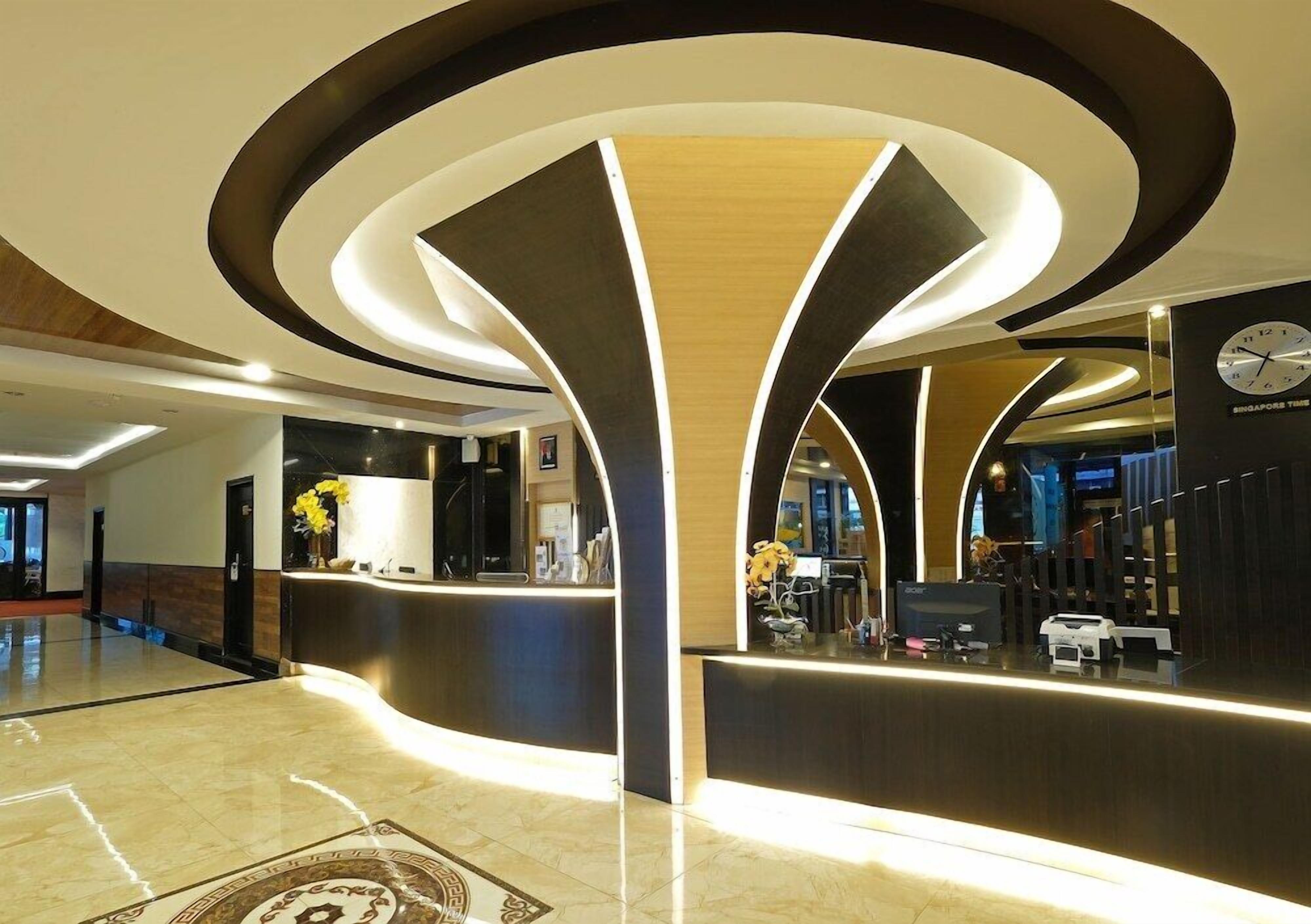 A modern hotel lobby with a curved reception desk, a clock on the wall, and a clean, polished floor.