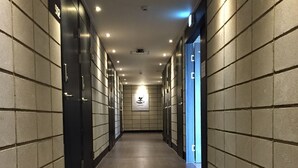 En lång, smal hall med kaklade väggar och ett trägolv, som leder fram till en dörr i slutet.